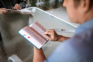 Two adults engaged in Bible study at a glass table outdoors, promoting faith and connection, and Grace