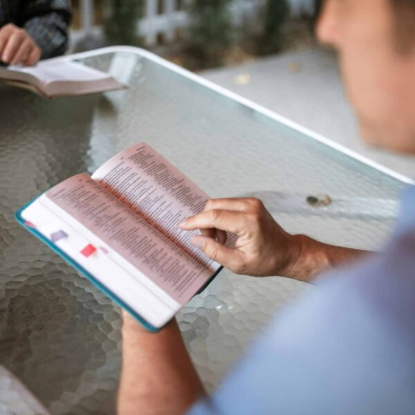 Two adults engaged in Bible study at a glass table outdoors, promoting faith and connection, and Grace