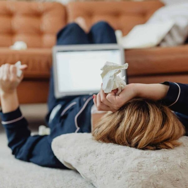 seasonal allergies, A woman in pajamas lies on the floor next to a laptop, surrounded by tissues, depicting a sick day at home.