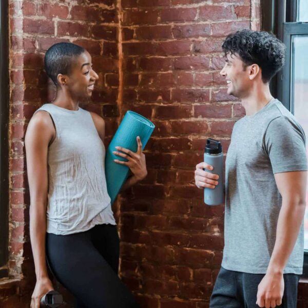 This photograph features a conversation between two people prepared for yoga class. At a gym, flirting can be a possibility between people who find connection.