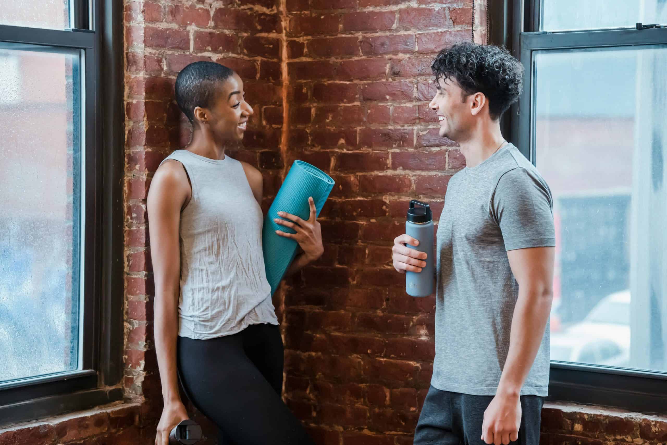 This photograph features a conversation between two people prepared for yoga class. At a gym, flirting can be a possibility between people who find connection.