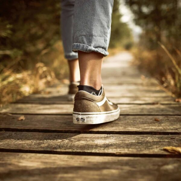 Person wearing sneakers walking on a wooden path in a sunlit park. Japanese walking trend.