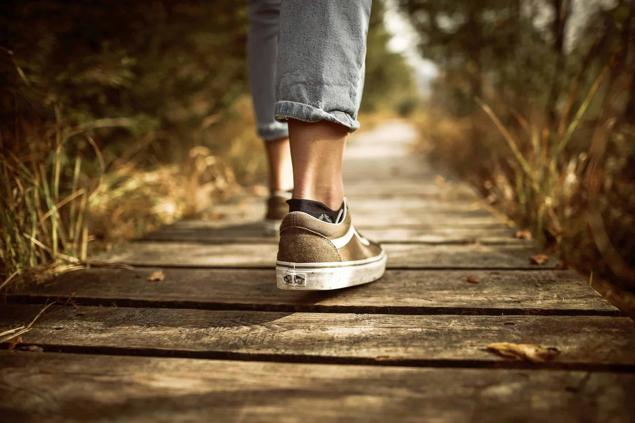 Person wearing sneakers walking on a wooden path in a sunlit park. Japanese walking trend.