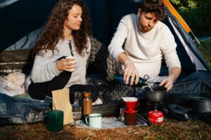 A couple brewing coffee with a chemex in a campsite, enjoying a relaxing outdoor experience. campsite safety