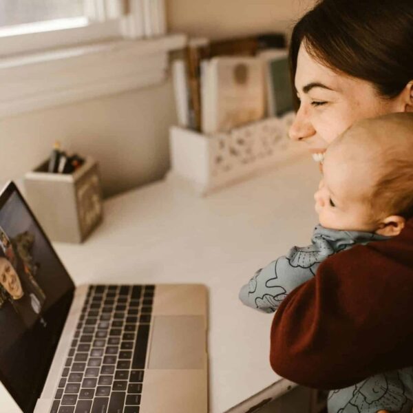 A happy mother and her baby making a video call on a laptop to connect with a long-distance loved one from home.