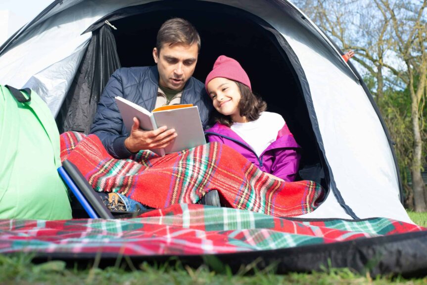 Father and daughter enjoy reading together in a cozy tent, capturing a moment of bonding in nature. camping activities for kids