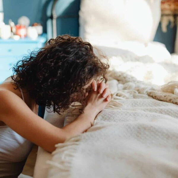 A woman kneels in contemplation by her bed, showcasing spirituality and tranquility in a warmly lit bedroom. morning routine