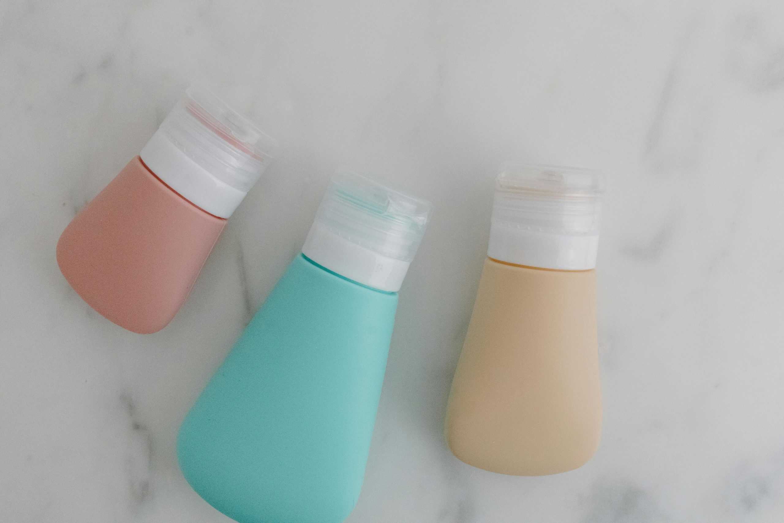 Three colorful squeezable bottles with flip tops on a marble surface.