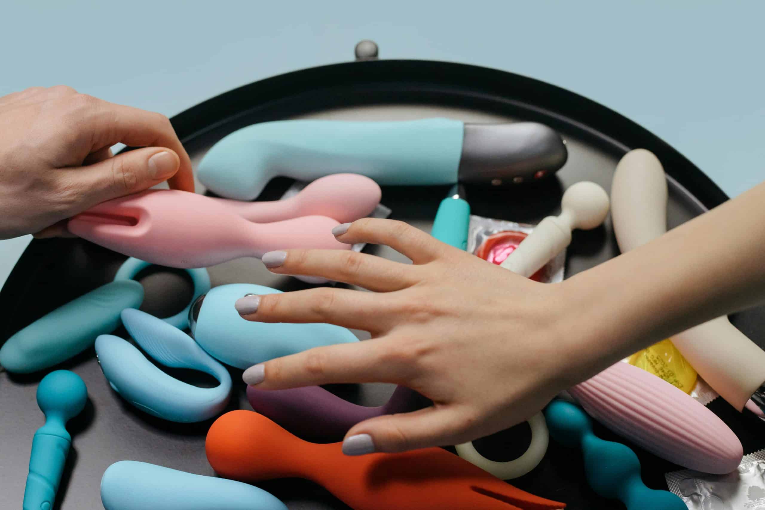 An assortment of vibrant sex toys with hands reaching for selection. vibrators