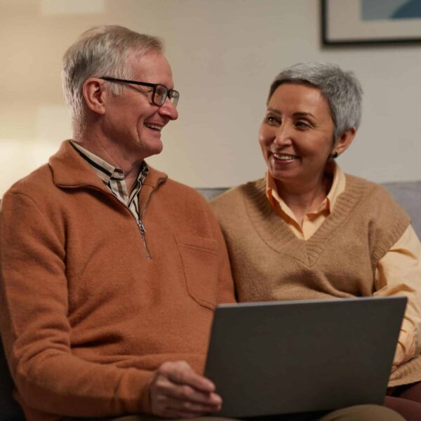 Senior couple smiling and using a laptop together in a cozy living room. Healthy patterns