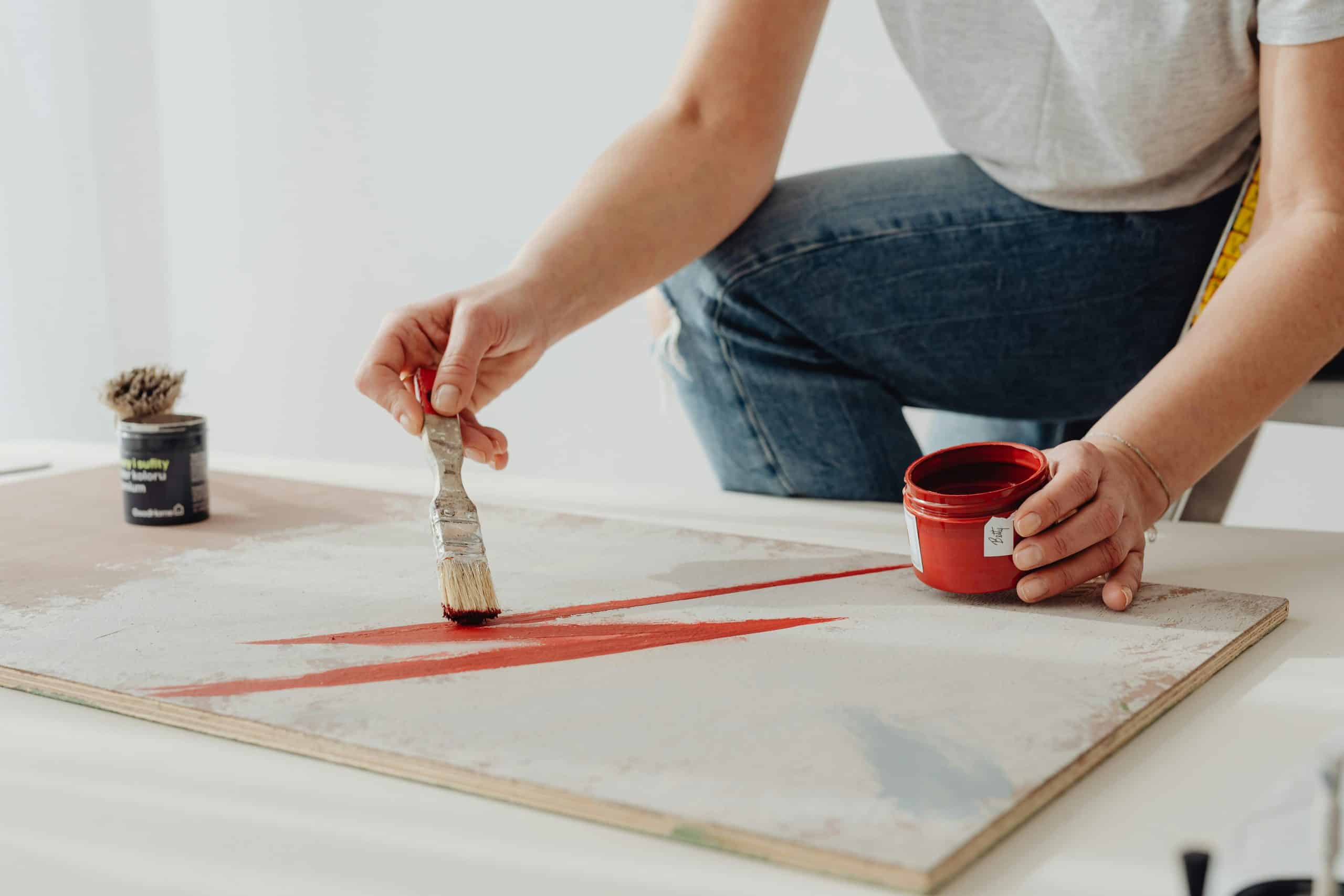 Home Upgrade: A person painting a red stroke on a board with a brush and paint pot.