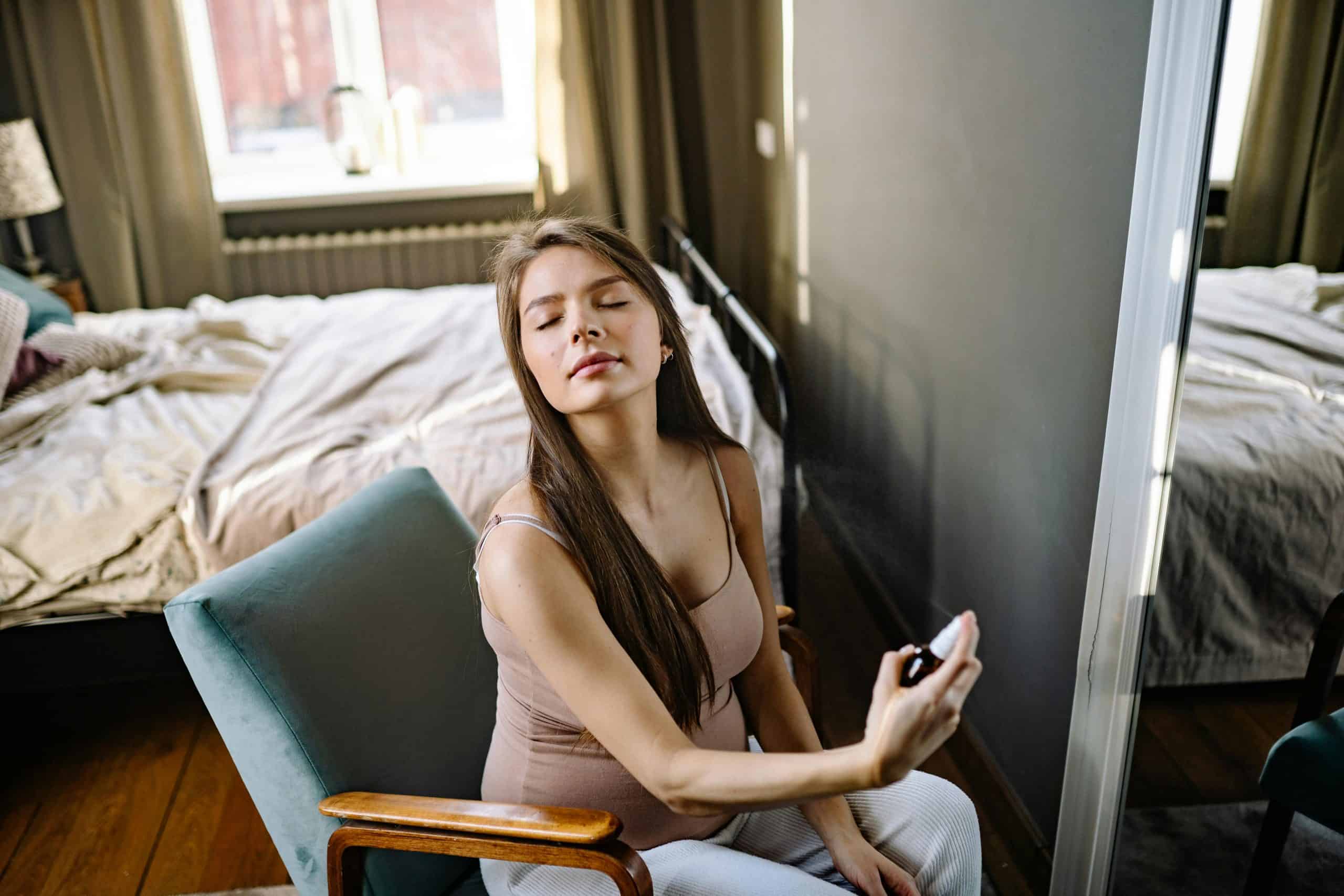 Pregnant woman sitting indoors, eyes closed, enjoying a refreshing fragrance. fragrances