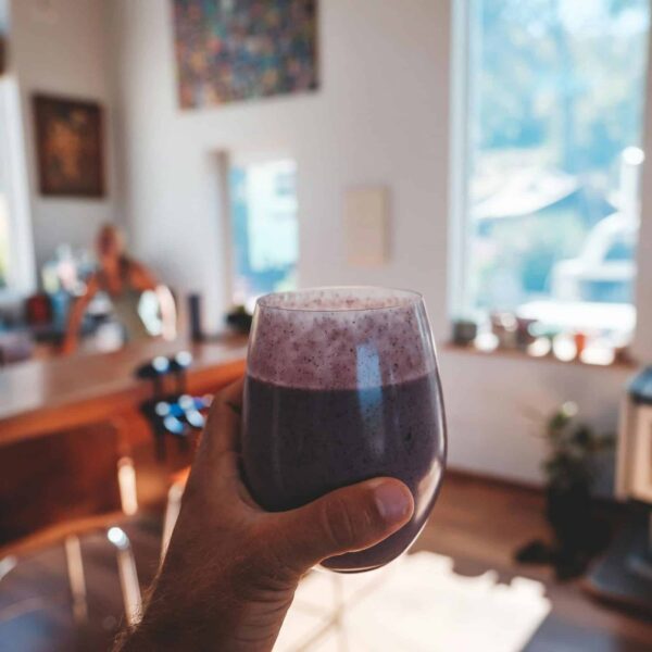Hand holding a fresh berry smoothie in a sunlit, cozy kitchen interior setting. Quick breakfast
