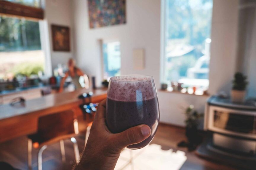 Hand holding a fresh berry smoothie in a sunlit, cozy kitchen interior setting. Quick breakfast