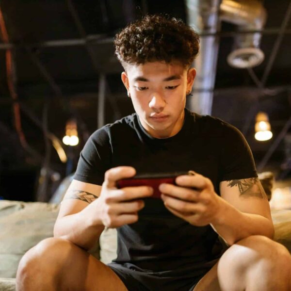 Focused young man engaged in gaming on smartphone indoors, enjoying online recreation. Depression treatment