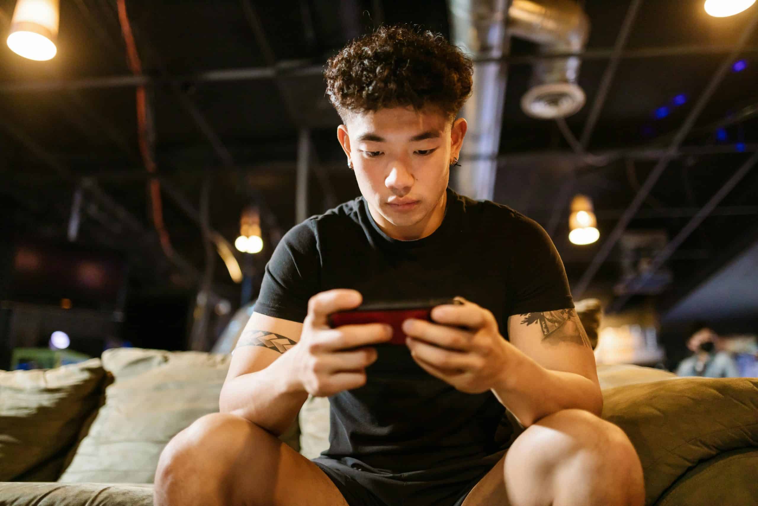 Focused young man engaged in gaming on smartphone indoors, enjoying online recreation. Depression treatment