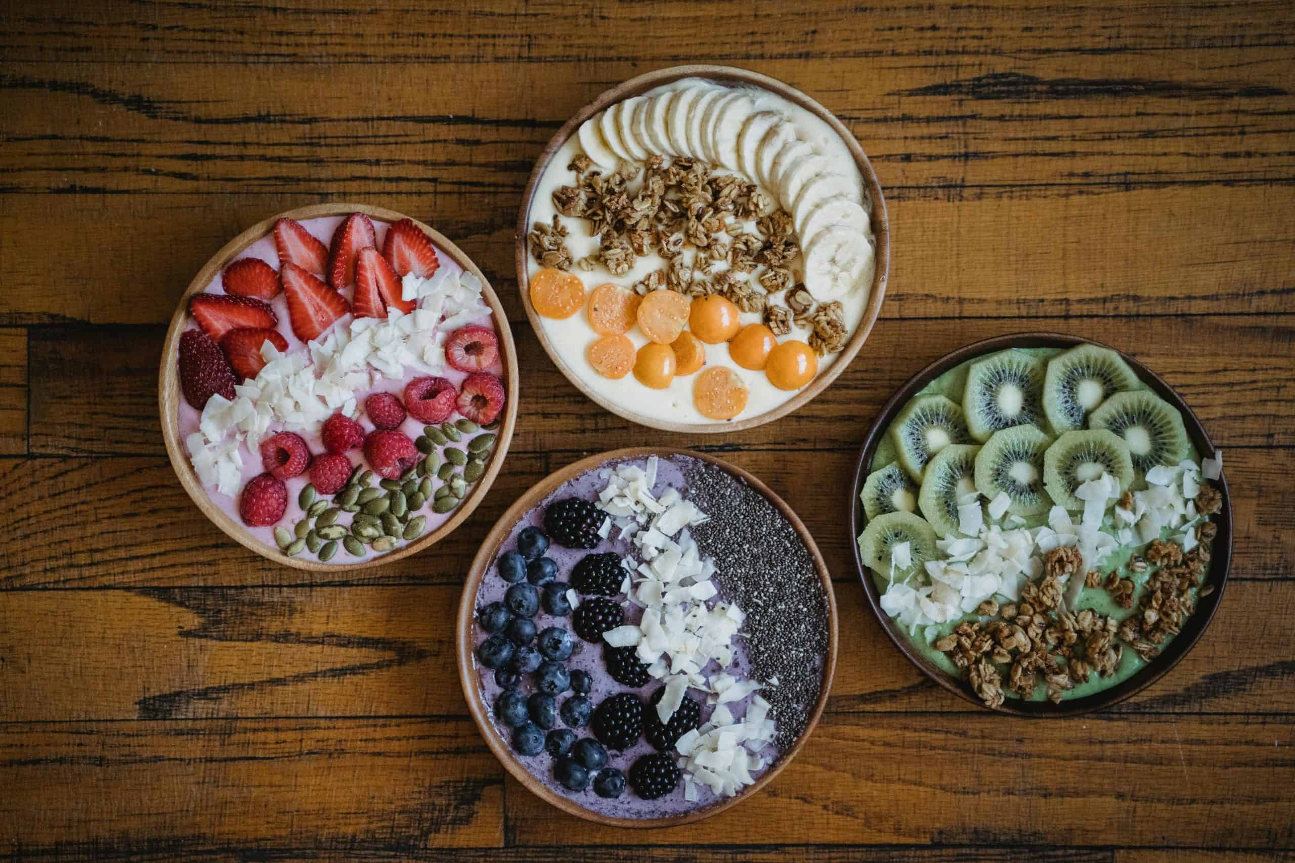 Four vibrant smoothie bowls with fruits, nuts, and granola on a wooden table. Gut health
