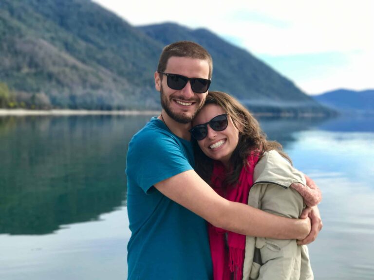 This photograph features a happy couple smiling in front of a lake. Going someplace new together can help you renew passion in your relationship.