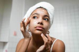 A young woman applies skincare cream in a modern bathroom setting., moisturizers