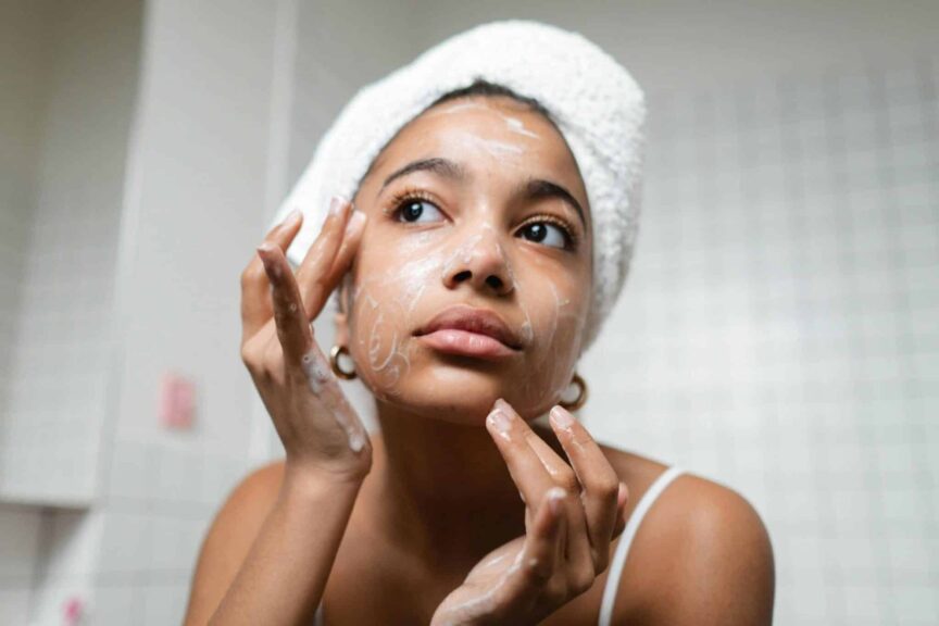 A young woman applies skincare cream in a modern bathroom setting., moisturizers