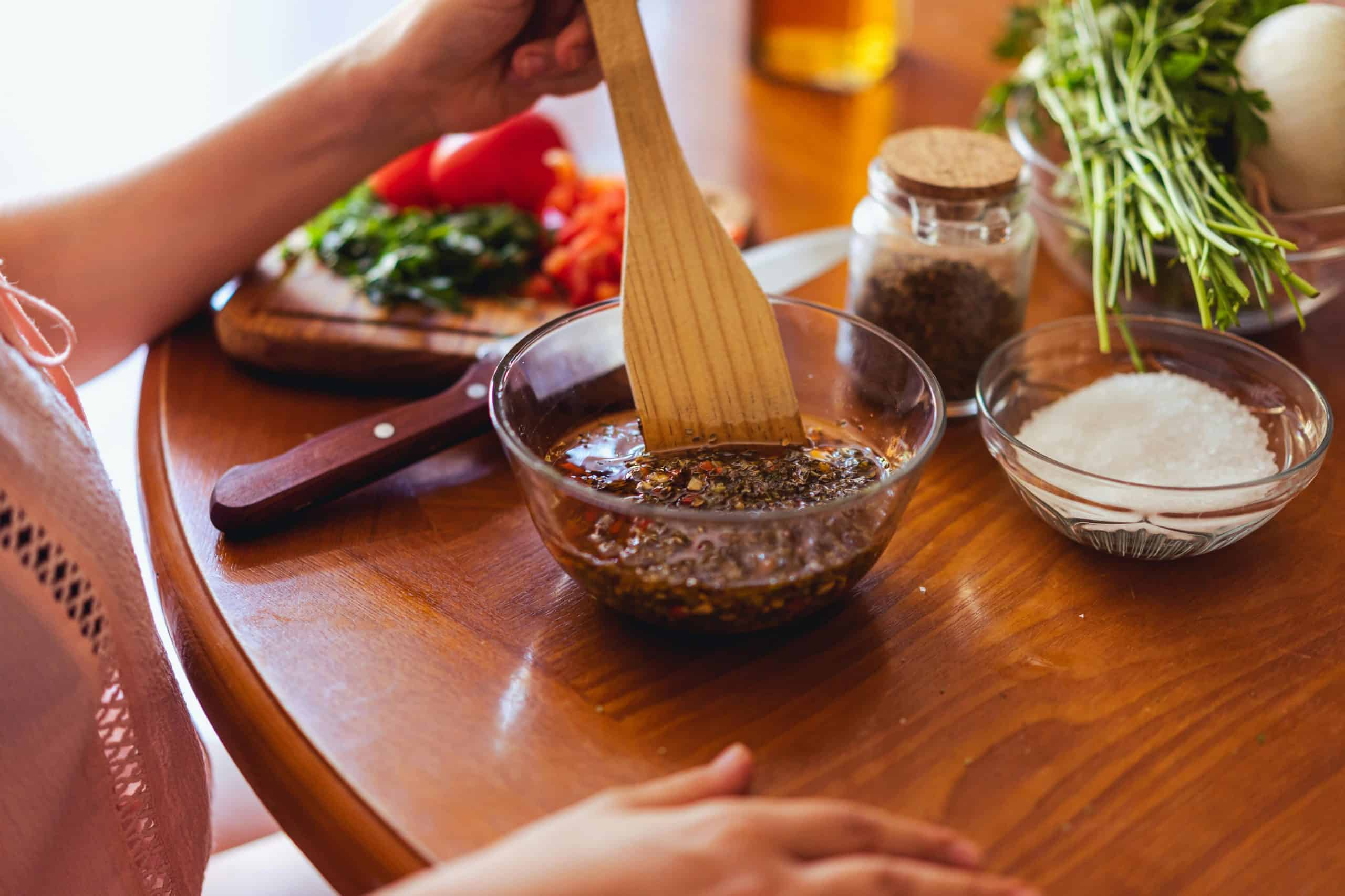 A person mixing chimichurri sauce with fresh herbs and spices in a kitchen setting.