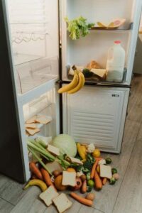 A messy open refrigerator with fresh vegetables and bread scattered on the floor. Going zero-waste