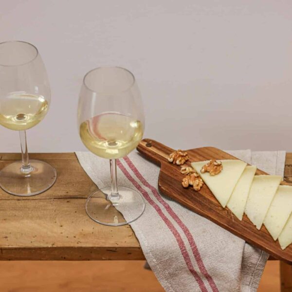 Sophisticated still life of white wine and sliced cheese with walnuts on a wooden board. Wine pairing