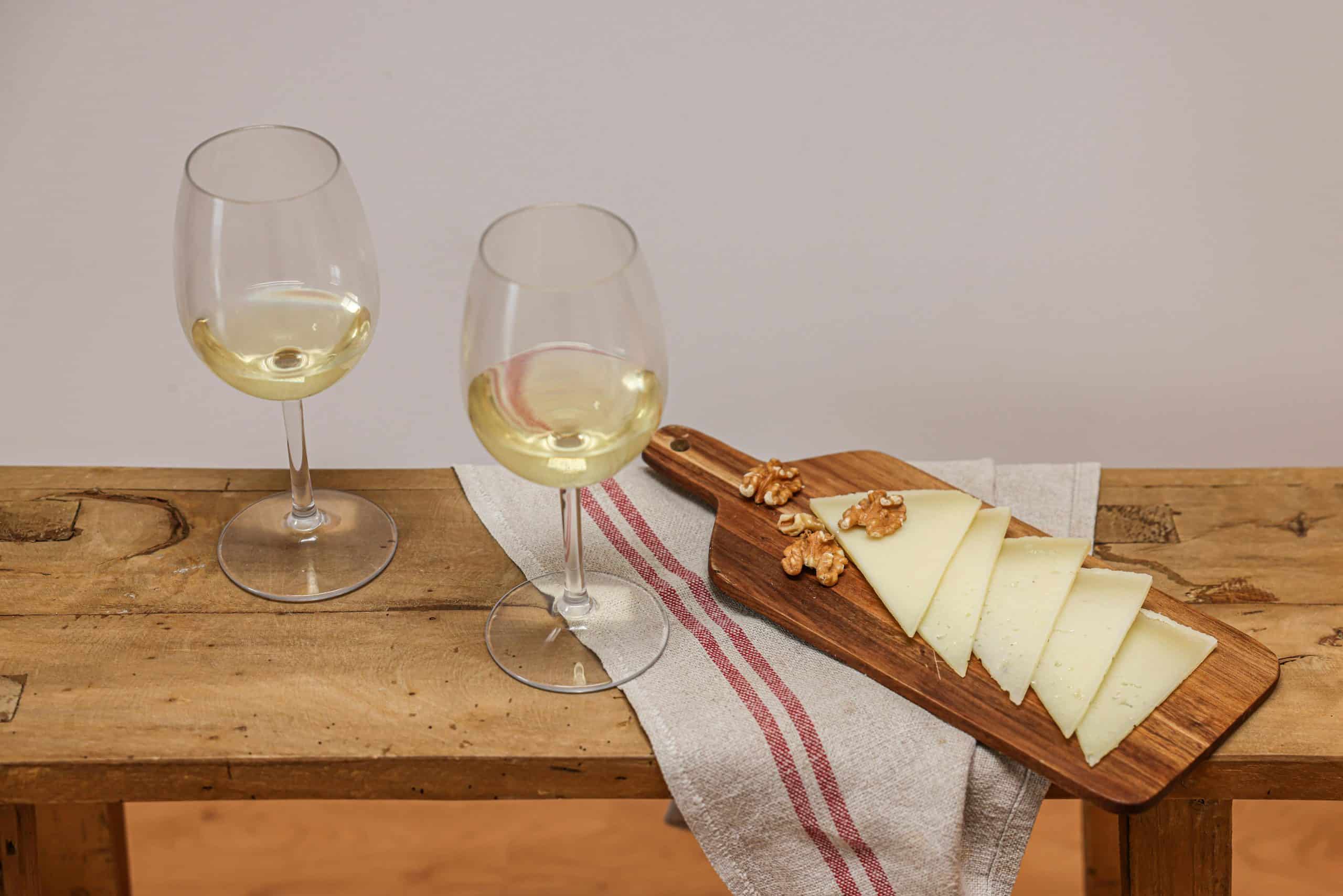 Sophisticated still life of white wine and sliced cheese with walnuts on a wooden board. Wine pairing