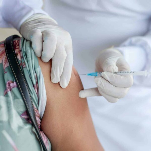 Close-up of a healthcare professional giving a vaccine shot to a patient wearing a mask. National immunization month