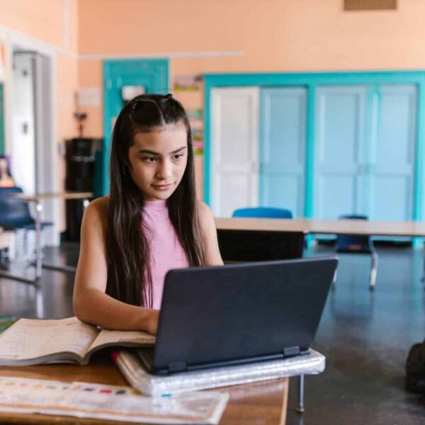 A focused young girl using a laptop for schoolwork in a bright classroom environment. back to school tech