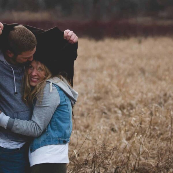 A couple shares a warm embrace under a coat in a rustic autumn field, expressing love and togetherness. interdependence