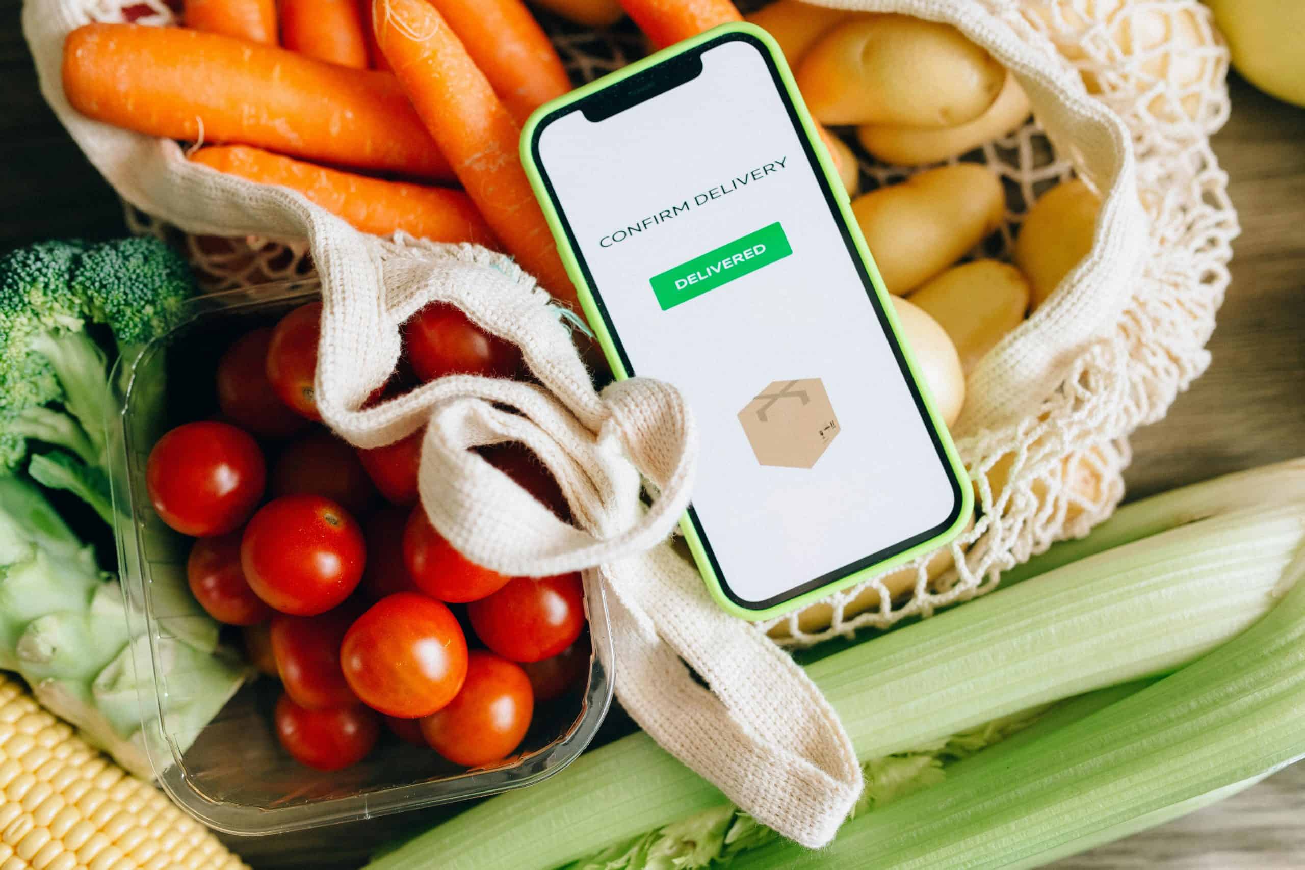 This photo contains fresh produce, a carrying bag, and confirmation of delivery via phone. Vegan meal delivery services can help make a vegan diet easier to maintain.