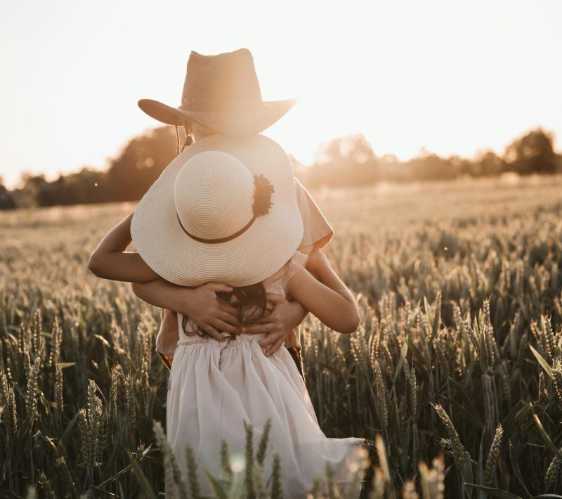 Unrecognizable boy and girl in hats hugging each other in field with cereal grass at sundown in countryside