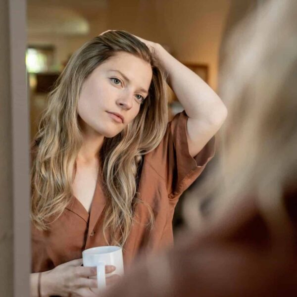 This photo is of a woman looking into a mirror and holding a coffee mug. You can check out your reflection throughout your day and use oil-blotting sheets as needed.