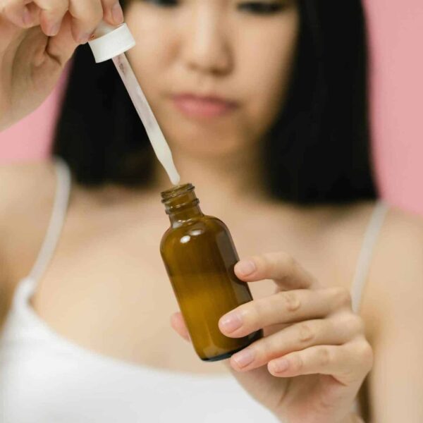 Close-up of a woman applying skincare serum with a pipette against a pink background. Hyaluronic acid