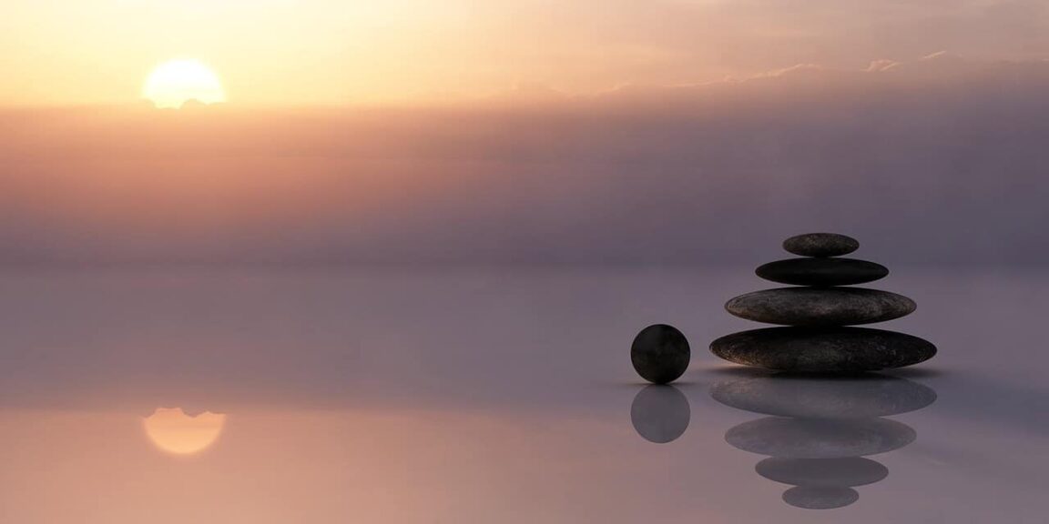 Stack of stones balanced at sunset with their reflection mirrored in calm water, symbolizing hormonal balance, wellness, meditation, and zen in nature. Image Credit: realworkhard via pixabay