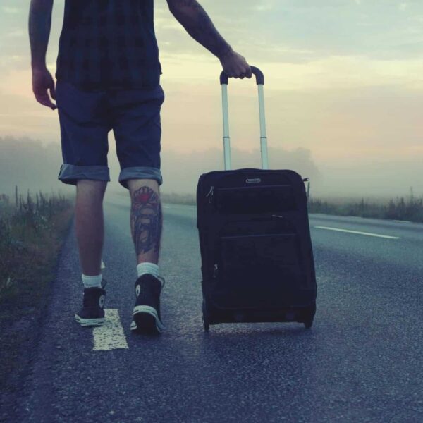 rolling suitcase ban, europe, Man walking with a suitcase along a foggy road at sunrise, symbolizing adventure and travel.