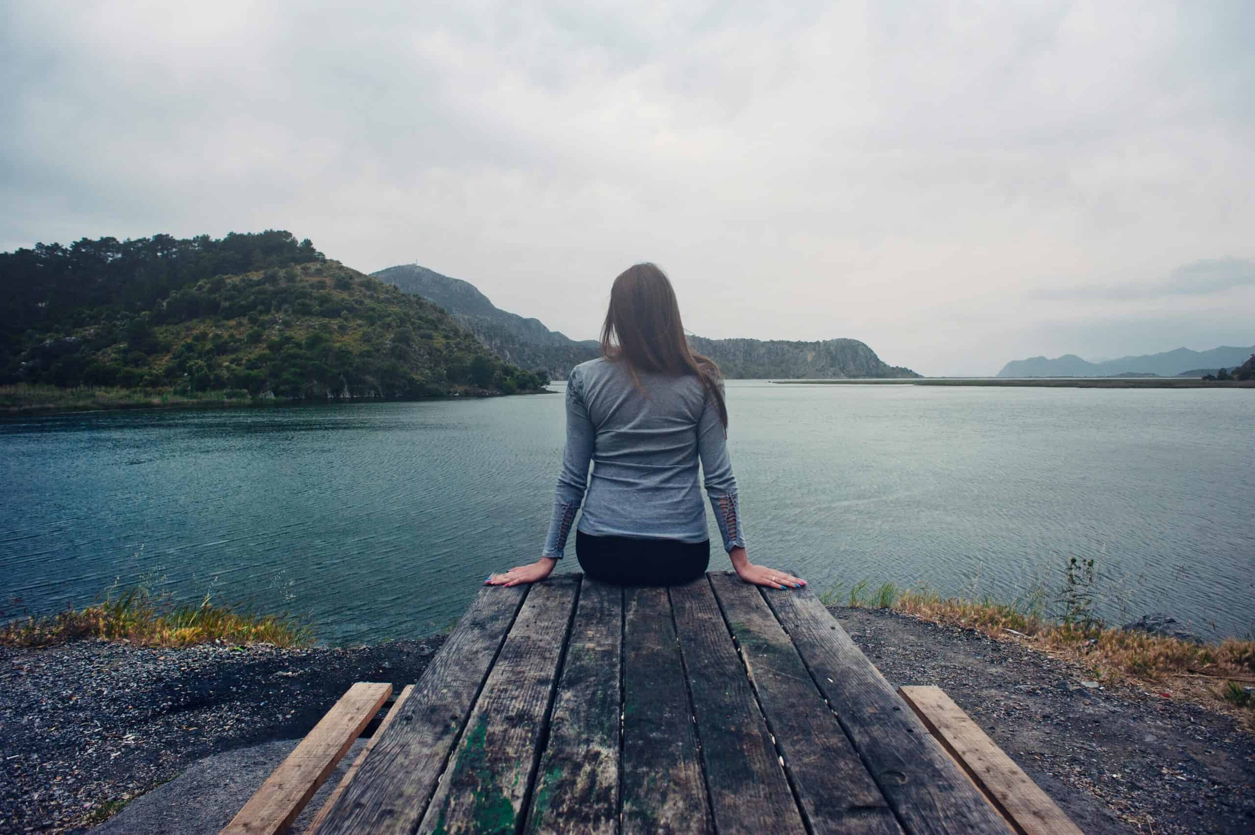 A woman sitting on wooden planks, enjoying a serene mountain lake view.