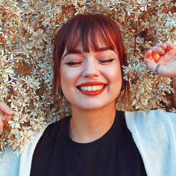 Redhead woman smiling with closed eyes, surrounded by blooming flowers, radiating joy and happiness. Beauty trends, fall 2025,