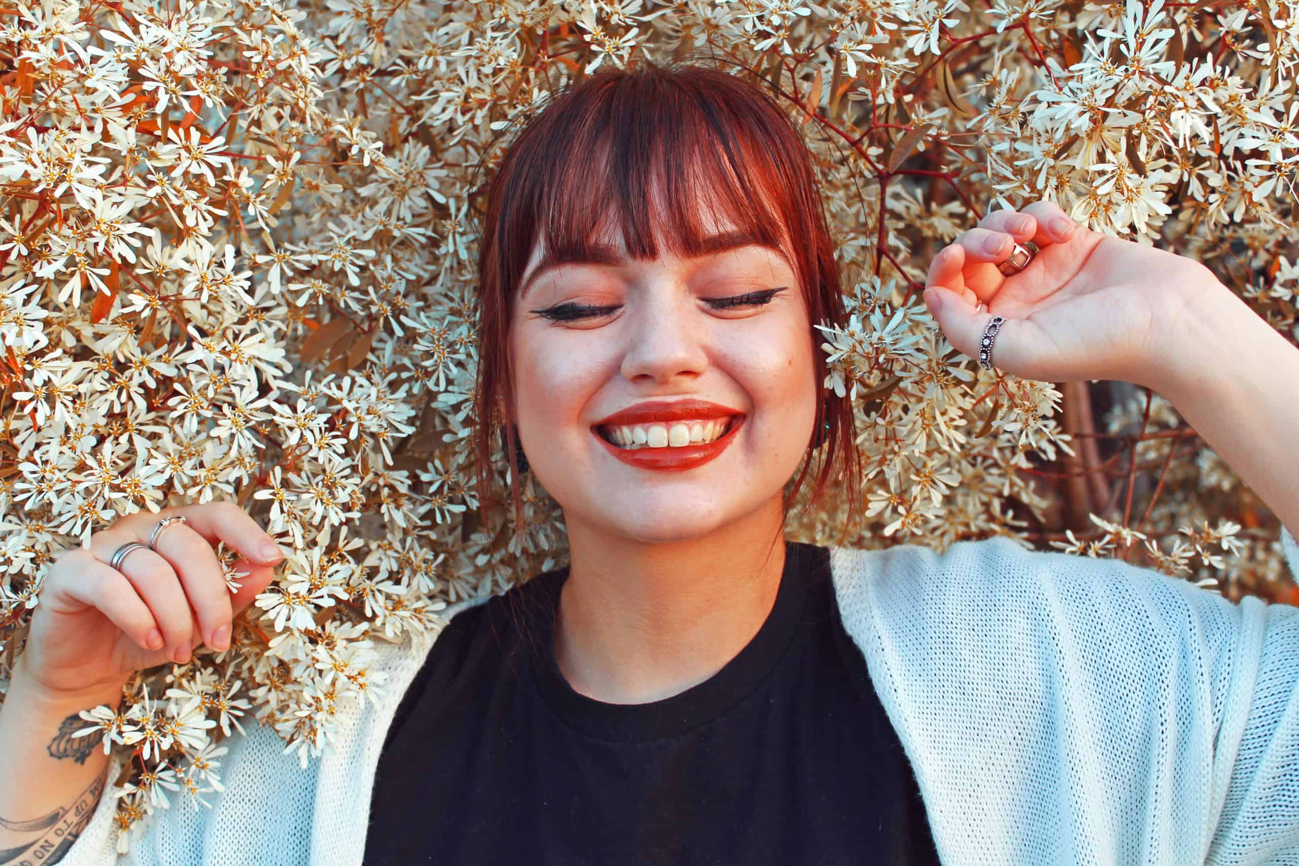 Redhead woman smiling with closed eyes, surrounded by blooming flowers, radiating joy and happiness. Beauty trends, fall 2025,