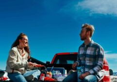 A cheerful couple having a picnic on a truck tailgate under clear blue skies. game day