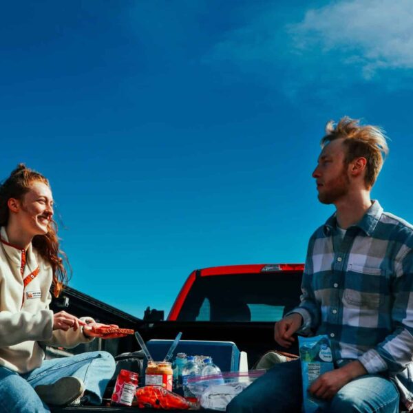 A cheerful couple having a picnic on a truck tailgate under clear blue skies. game day