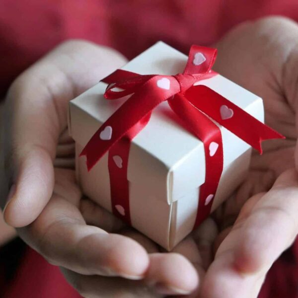 A heartfelt moment captured with hands holding a small gift box tied with a red ribbon, pebbling, friendships