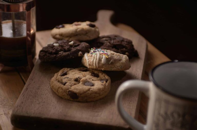 Delicious assorted cookies on a wooden board accompanied by coffee, perfect for a cozy snack time.