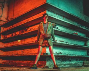 crossbody bags, bags for travel, Stylish woman in coat and sunglasses standing in industrial environment with dramatic lighting.