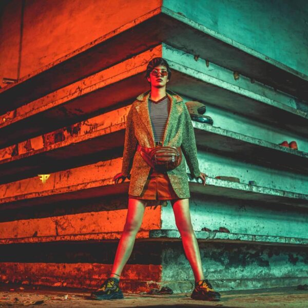 crossbody bags, bags for travel, Stylish woman in coat and sunglasses standing in industrial environment with dramatic lighting.