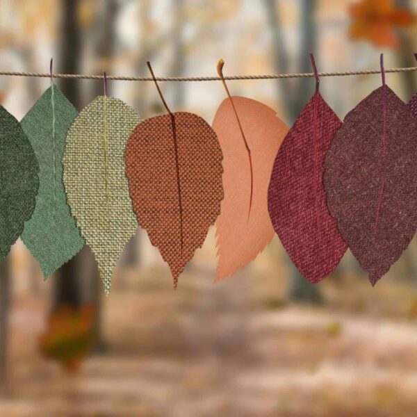 Fabric leaves hang on a rope, showcasing autumn colors in a forest backdrop. sustainable fall decor