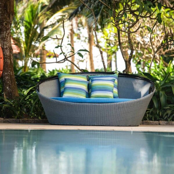 Inviting outdoor wicker chair with pillows, surrounded by lush plants by the poolside, backyard lounge