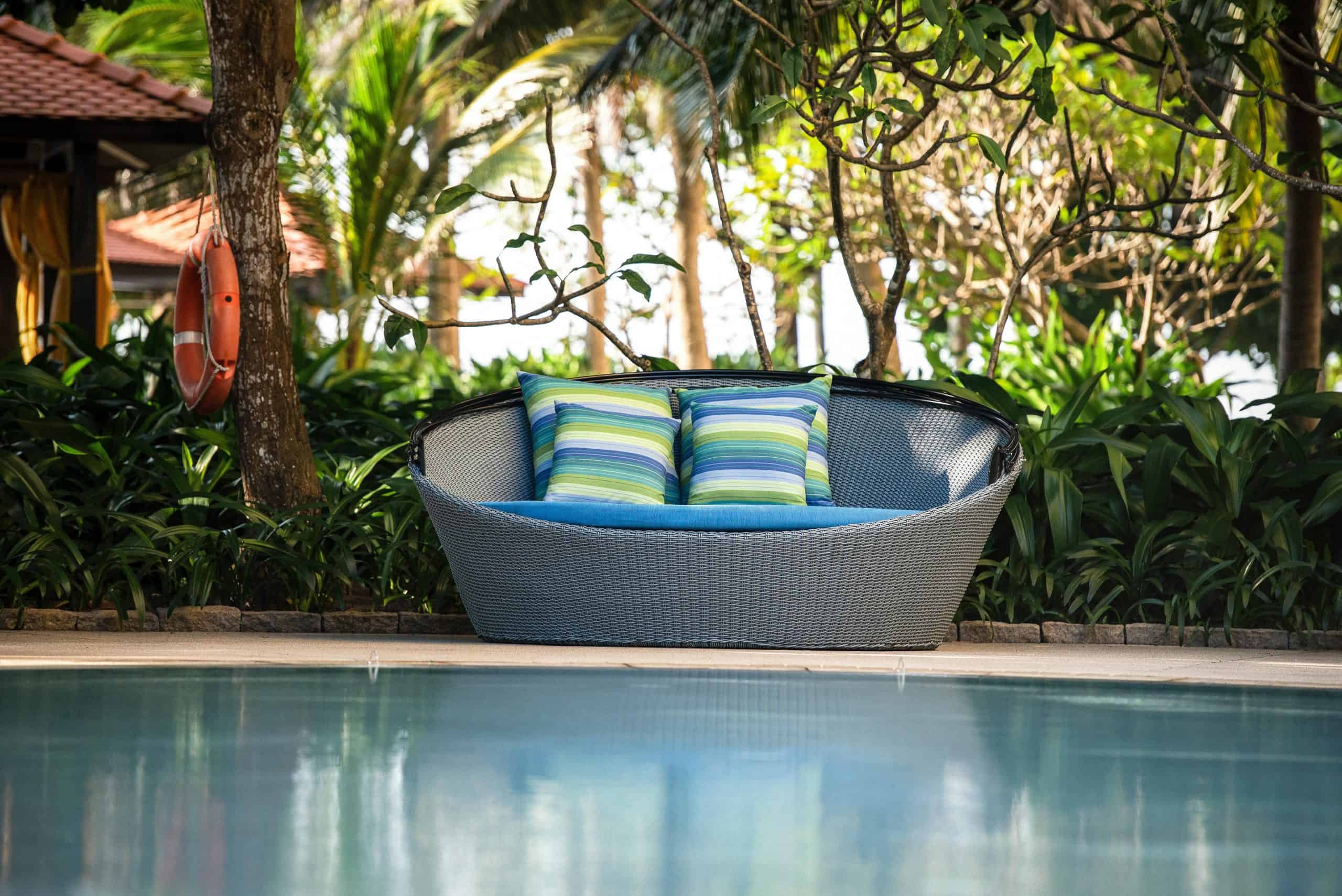Inviting outdoor wicker chair with pillows, surrounded by lush plants by the poolside, backyard lounge
