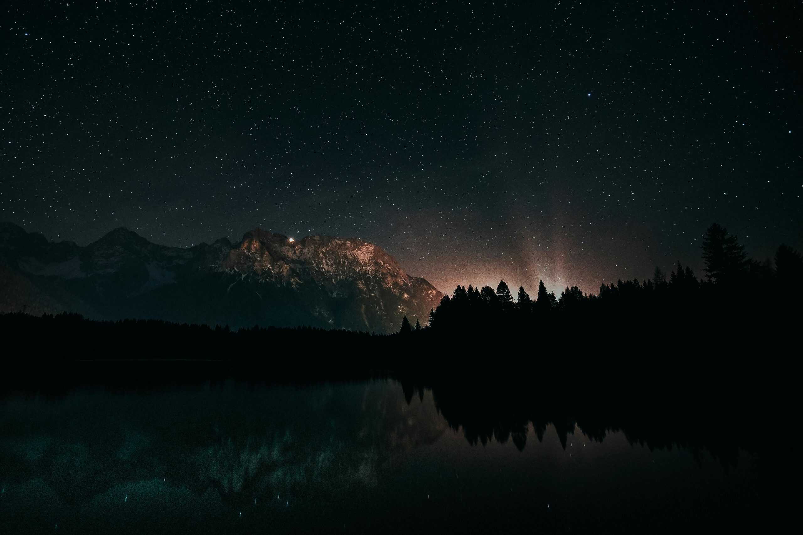 Beautiful starry night with mountains and forest reflecting on calm water